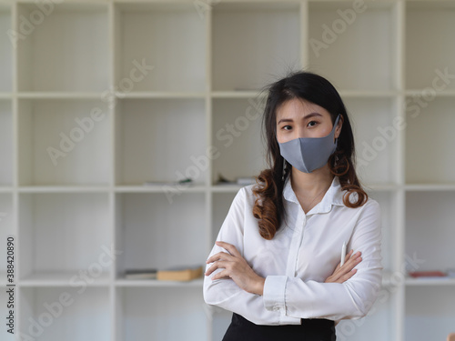 Businesswoman standing with arms crossed in the office room and wearing a face mask