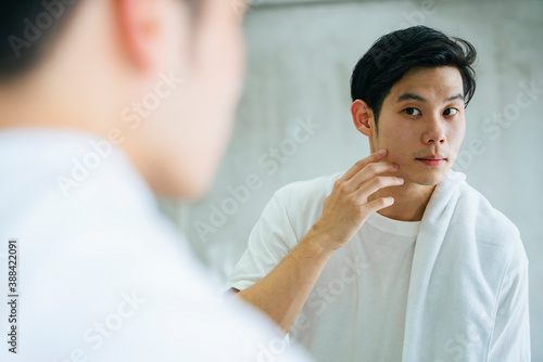 Young man looking himself in bathroom mirror.