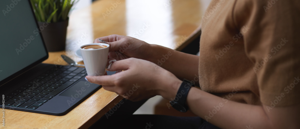 Female hand holding coffee cup while sitting at workplace in cafe Female hand holding coffee cup while sitting at workplace in cafe