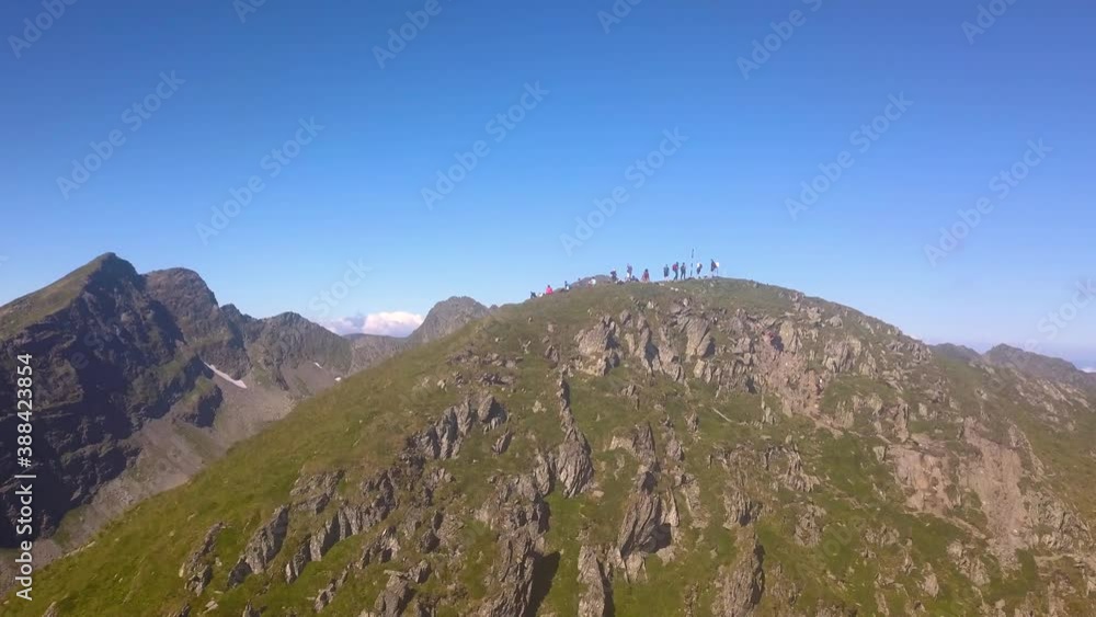 Descending aerial view of hikers on mountain summit looking out over vast majestic landscape with blue sky. Success, achievement and outdoor adventure concept. Drone view of climbers on mountain top. Descending aerial view of hikers on mountain summit looking out over vast majestic landscape with blue sky. Success, achievement and outdoor adventure concept. Drone view of climbers on mountain top.