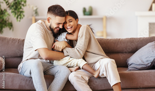 happy multi ethnic family mother father and son having fun at home on couch .