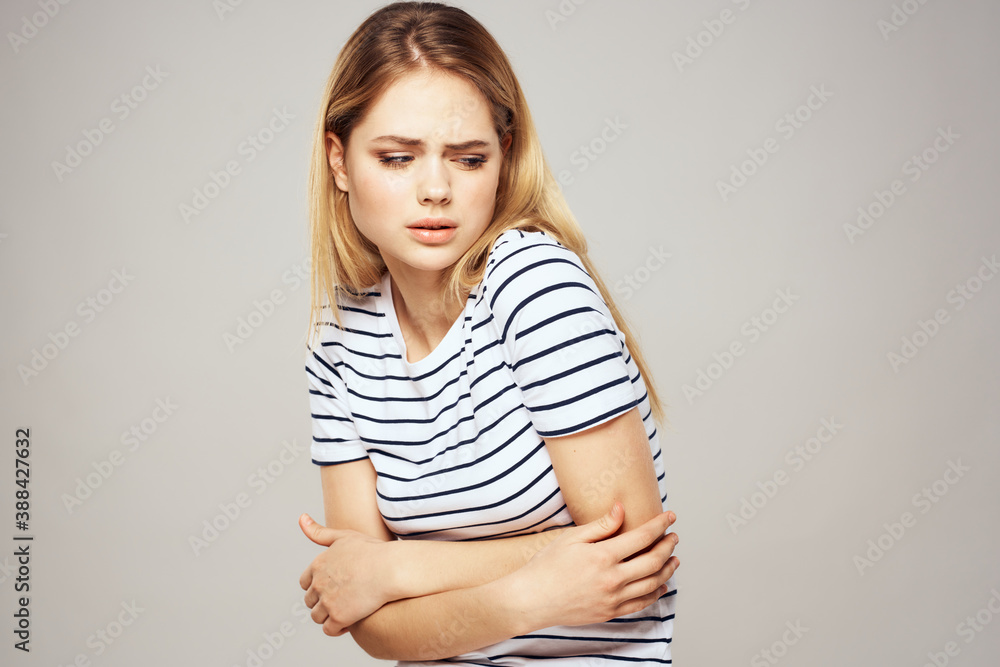 A woman in a striped T-shirt holds her hands in front of her emotions displeasure light background A woman in a striped T-shirt holds her hands in front of her emotions displeasure light background