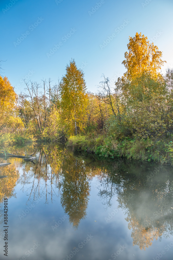 Autumn forest is reflected in the water of river with fog on the water Autumn forest is reflected in the water of river with fog on the water