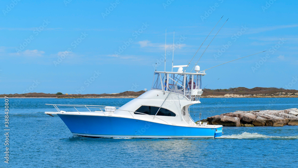 Fototapeta premium Beautiful blue and white fishing yacht boat sails on the calm blue water as it leaves the marina on a sunny day.