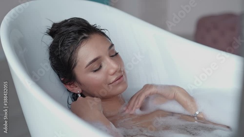 Close up relaxed woman touching skin with foam in bath. Top view of sexy girl taking bathtub at home. Romantic brunette woman relaxing bath in slow motion.