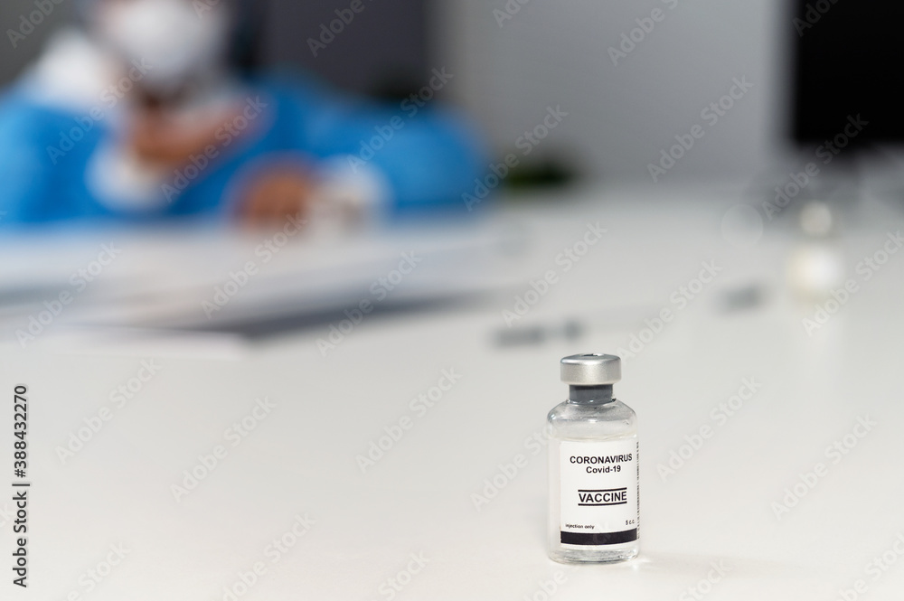 Coronavirus covid 19 vaccine sample in a clean laboratory meeting room with a background of coronavirus covid 19 disease experts discussion with protective suit, mask and gloves Coronavirus covid 19 vaccine sample in a clean laboratory meeting room with a background of coronavirus covid 19 disease experts discussion with protective suit, mask and gloves