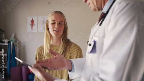 Caucasian young female patient looking at doctor showing her medical report on digital tablet