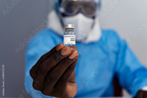 Coronavirus covid 19 disease experts hold samples of coronavirus covid 19 vaccine sample labelled coronavirus covid 19 with confidence and protective suit, mask and gloves