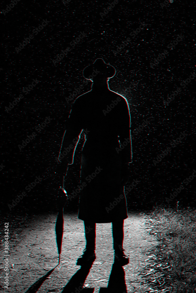 dark silhouette of a man in a raincoat and hat under an umbrella on the street in the rain dark silhouette of a man in a raincoat and hat under an umbrella on the street in the rain
