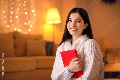 Beautiful young woman with book at home on Christmas eve