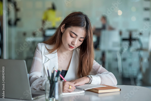 Beautiful asian businesswoman or financial manager working in modern office on laptop. Businesswoman working on laptop and taking note while sitting at the table in office.