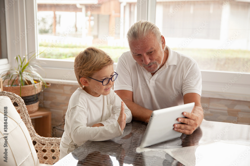 Happy family senior and little boy using tablet for conversation with their relatives or friends, waving hands and say Hello. Grandson and grandfather having video chat using tablet. Happy family senior and little boy using tablet for conversation with their relatives or friends, waving hands and say Hello. Grandson and grandfather having video chat using tablet.