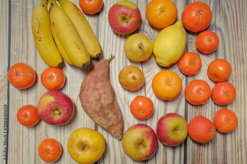 Many different autumn fruits on a wooden board like mandarins, lemos, apples and bananas