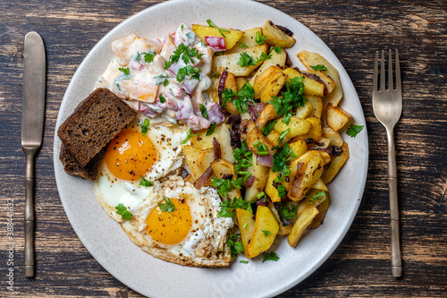 Ukrainian food, fried potatoes with onions, eggs, vegetable salad, black bread on wooden background