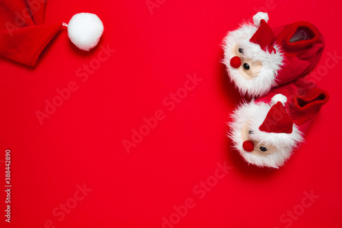 New year, Christmas slippers in form of santa claus with white soft fur on red background with place for text. Funny, cozy, fluffy children shoes. Warm and original gift for the winter holidays