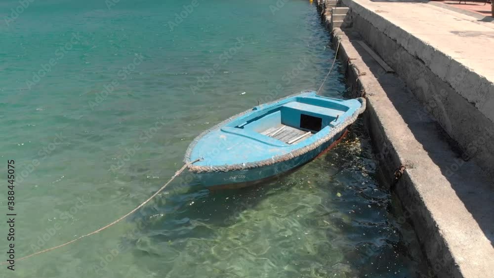 A lone rustic blue wooden rowboat gently bobs in the warm clear harbor waters, Croatia, Adriatic Sea A lone rustic blue wooden rowboat gently bobs in the warm clear harbor waters, Croatia, Adriatic Sea