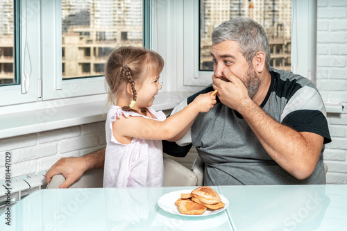 a cute little girl laughingly presents cooked pancakes to her gray-haired dad. father jokingly refuses to eat. family values and the concept of joint leisure