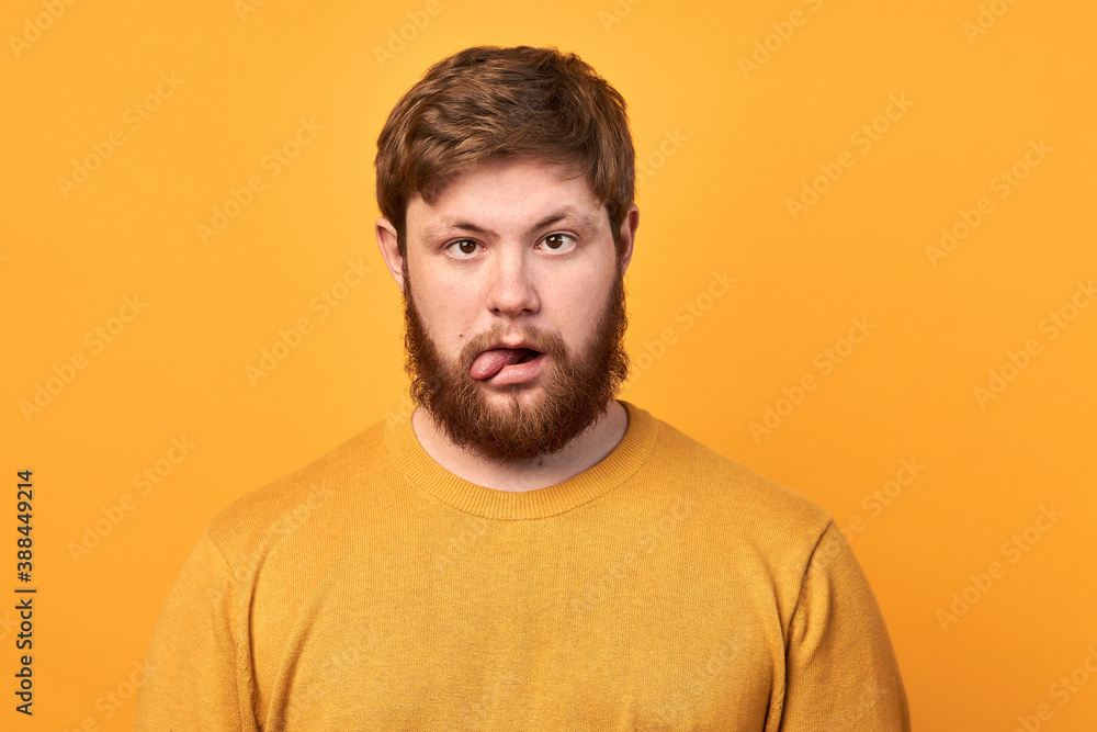 Excited bearded man looking at the camera with sidelong eyes, isolated on yellow background. crazy guy stuck out his tongue Excited bearded man looking at the camera with sidelong eyes, isolated on yellow background. crazy guy stuck out his tongue