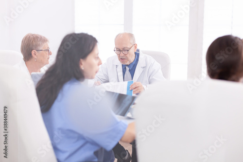 Mature doctor reading health raport during meeting with coworkes in hospital conference room. Clinic expert therapist talking with colleagues about disease  medicine professional