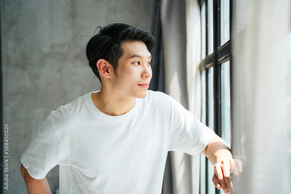 Young man in white shirt looking outside the window at home. Young man in white shirt looking outside the window at home.