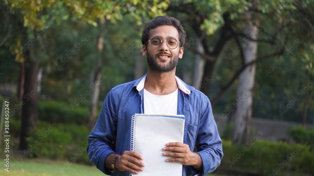 Handsome young indian student man read notebooks while standing on Collage Campus Handsome young indian student man read notebooks while standing on Collage Campus