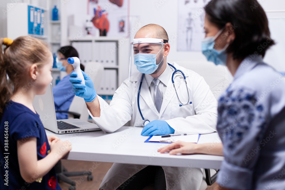 Fototapeta premium Doctor wearing face mask against coronavirus checking temperature using digital thermometer on child during medical examination. Health pediatrician specialist providing health care services.