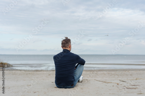 Man sitting on a sandy beach looking out to sea