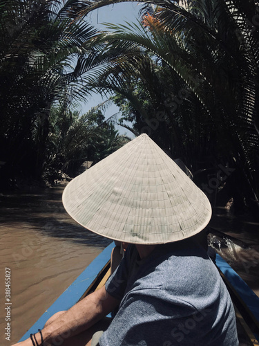 Boy in a boat with traditional Vietnamese hat through the Mekong delta river, Vietnam