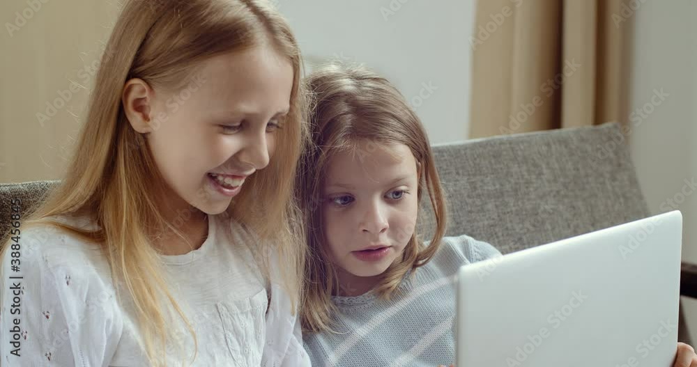 Two cute little preschool children friends girl laughing watching online cartoons video movie together, happy kids sisters learn use laptop computer sit on sofa at home, children technology concept Two cute little preschool children friends girl laughing watching online cartoons video movie together, happy kids sisters learn use laptop computer sit on sofa at home, children technology concept