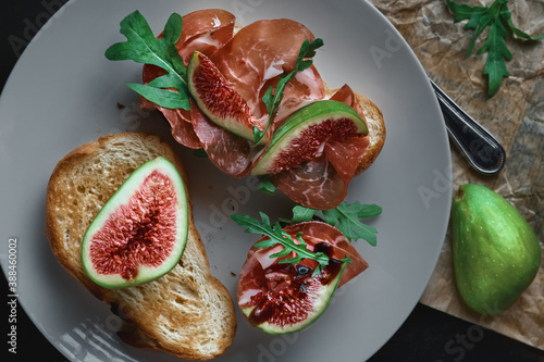 Bruschetta with prosciutto ham, ricotta cheese, arugula and fresh figs on a plate. appetizing appetizer. Flat lay. Starters or snacks concept
