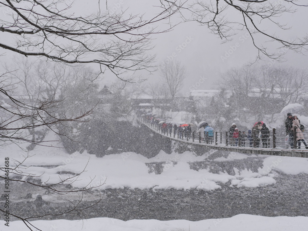 Tourists are walking across the bridge to go to Shirakawa-go village. On a snowy day
