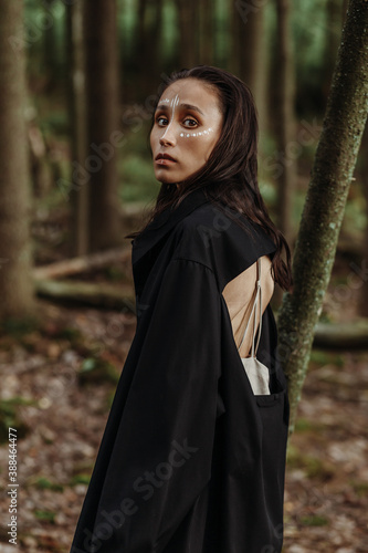 Pretty young mixed race woman with native make-up posing in the rain forest in a black stylish tunic.