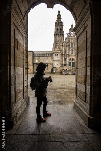 Young woman wearing a coat looking at her photo camera next to the cathedral of Santiago de Compostela.