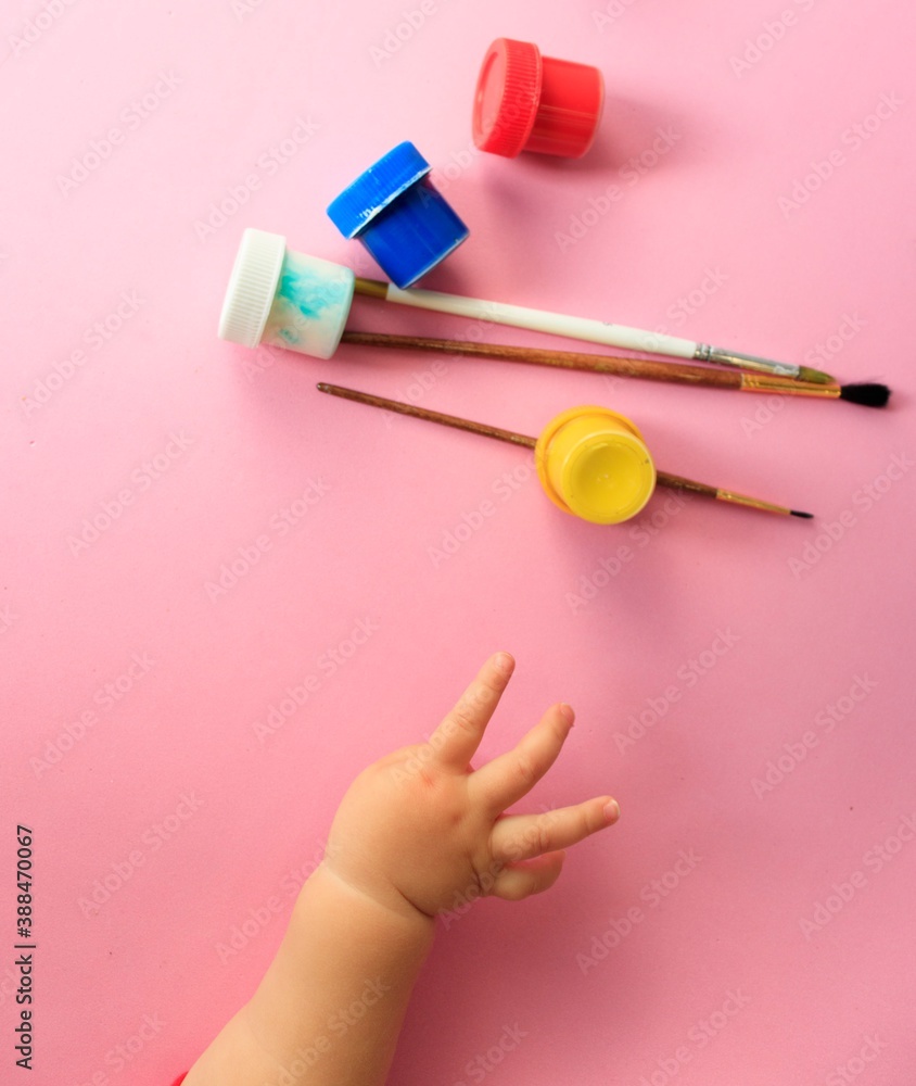 a child's hand holds brushes and paints on a pink background top view with space for text a child's hand holds brushes and paints on a pink background top view with space for text