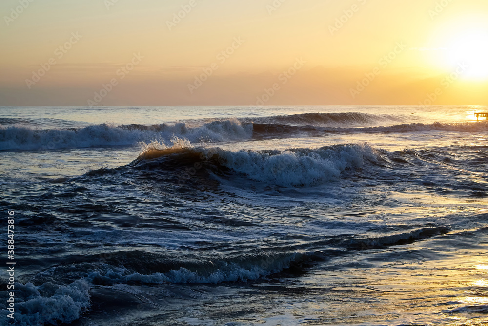 Water of sea with waves and yellow sky at sunset.