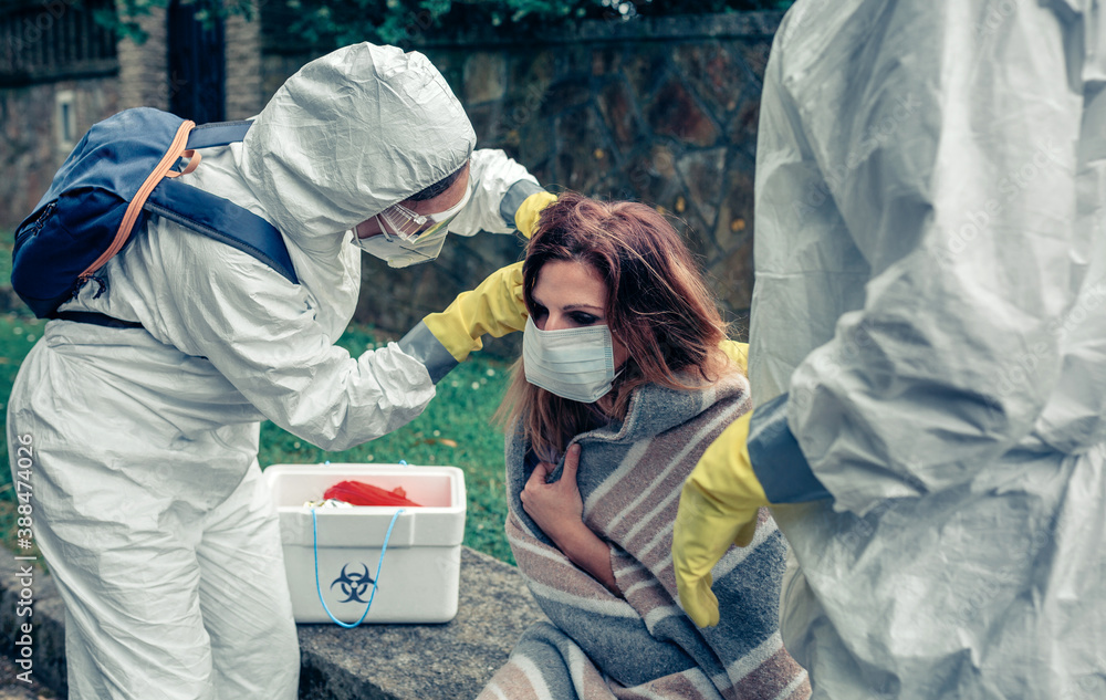 Doctors putting protective mask on woman infected by a virus outdoors