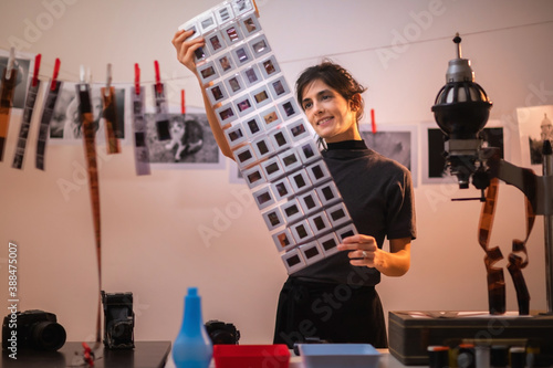 Young creative female holding frames of diapositive in darkroom. Portrait of creative girl photographer in photo studio darkroom. Developing analog camera film