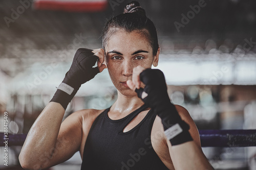 Obraz na płótnie Portrait of a woman standing in striking pose and looking at camera at dark ring. Portrait of woman kickboxer ready to punch. Muay thai concept w salonie