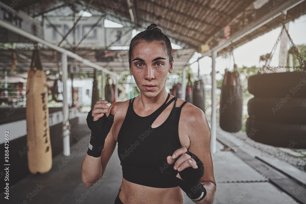 Portrait of a woman standing in striking pose and looking at camera at dark ring. Portrait of woman kickboxer ready to punch. Muay thai concept