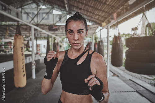 Obraz na płótnie Portrait of a woman standing in striking pose and looking at camera at dark ring. Portrait of woman kickboxer ready to punch. Muay thai concept w salonie