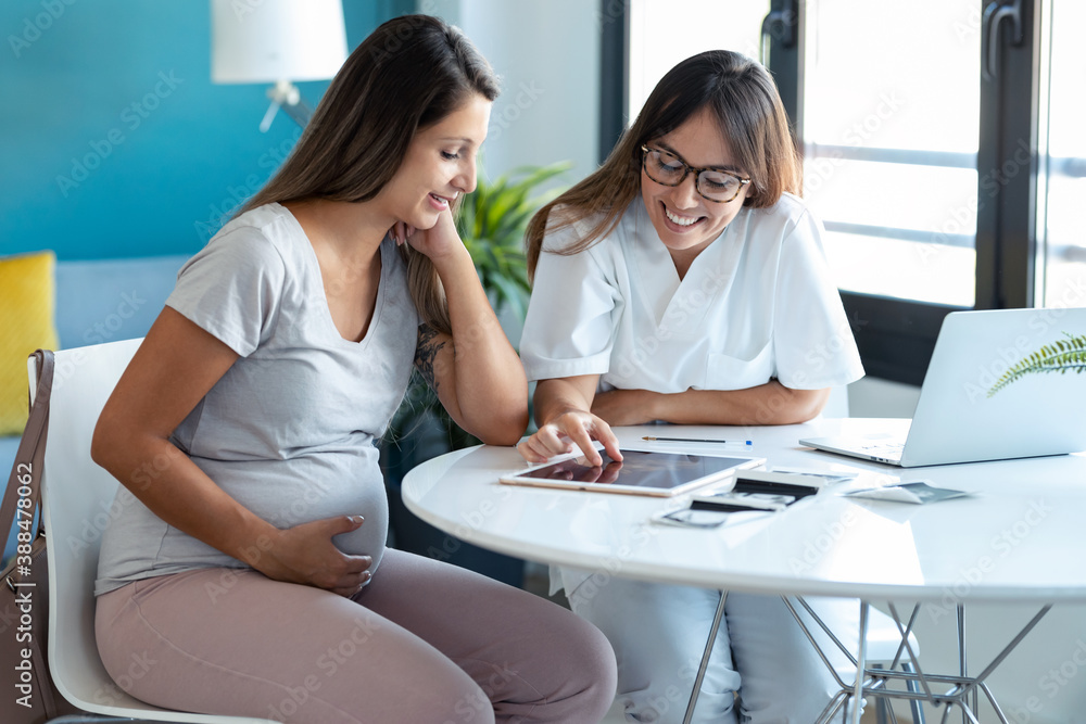 Young woman gynecologist doctor showing to pregnant woman ultrasound scan baby with digital tablet in medical consultation. Young woman gynecologist doctor showing to pregnant woman ultrasound scan baby with digital tablet in medical consultation.