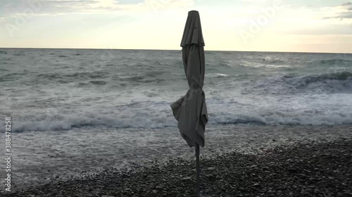 Storm at the sea coast. Closed beach umbrella, strong wind, big waves with lot of foam. Summer evening, bright dky and gray water. photo