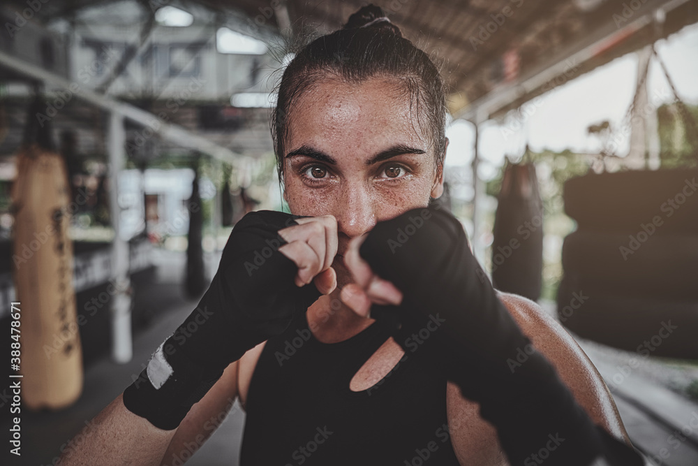 Portrait of a woman standing in striking pose and looking at camera at dark ring. Portrait of woman kickboxer ready to punch. Muay thai concept