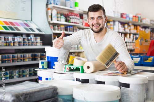 Fotografie Smiling guy demonstrating tools for house renovating in a paint supplies store