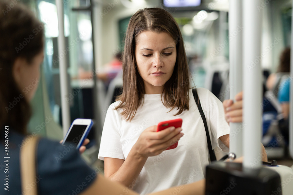 Young woman browsing and typing messages on phone on way to work in modern streetcar ..