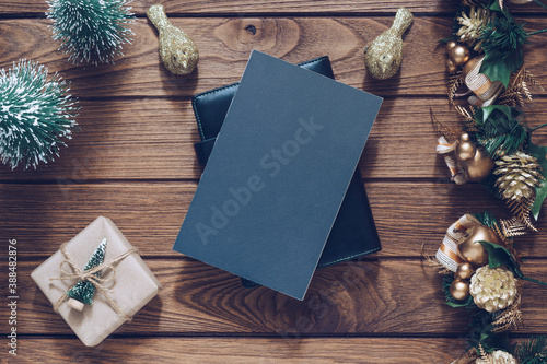 Mockup blank black book cover with Christmas gift box, Xmas ornaments and Christmas tree model decor on wooden table background. Flat lay, Top view with copy space