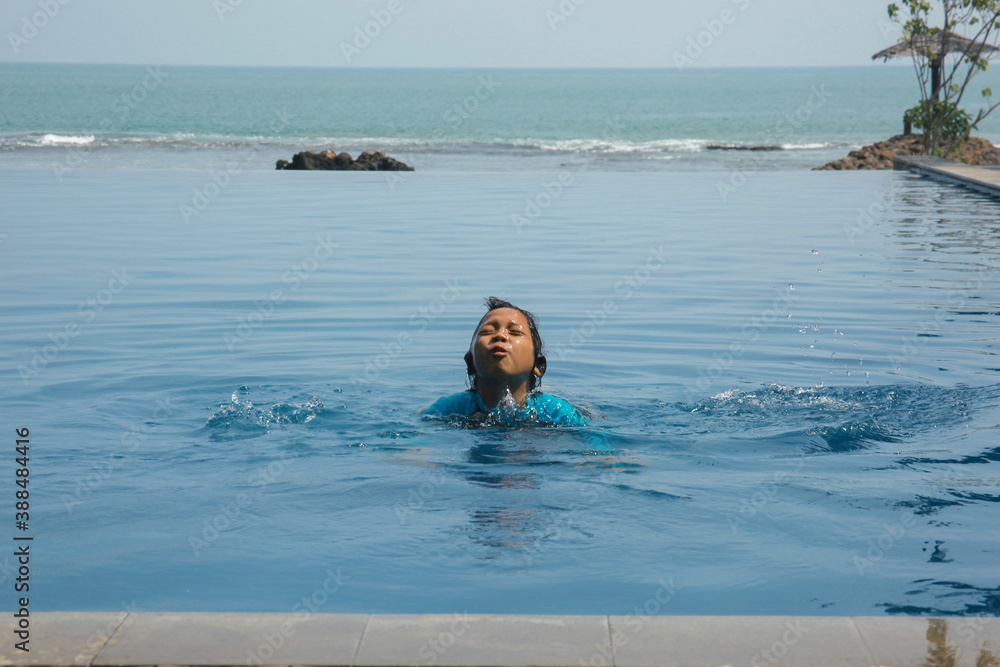 Joyful boy swimming on the infinity pool with sea view on the background Joyful boy swimming on the infinity pool with sea view on the background