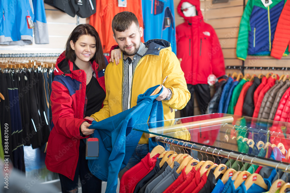 Fototapeta premium Young loving couple deciding on track jacket in sports clothes store