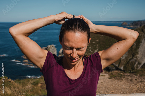 Athletic woman making herself a ponytail in the hair, with the coastline in the background