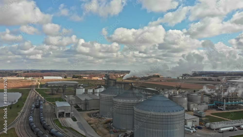 Aerial view of mill with steel silos for grain storage and processing plant, train tracks against beautiful rural countryside - drone ascending day Aerial view of mill with steel silos for grain storage and processing plant, train tracks against beautiful rural countryside - drone ascending day
